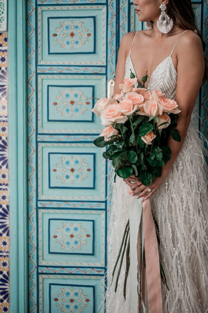 Bride holds bouquet of pink roses against turquoise door at Be Riad in Marrakech