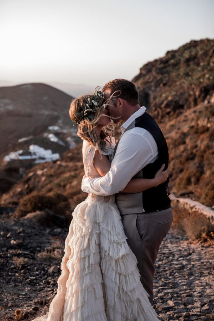 Bride and groom embrace on cliffsides of Greece at sunset
