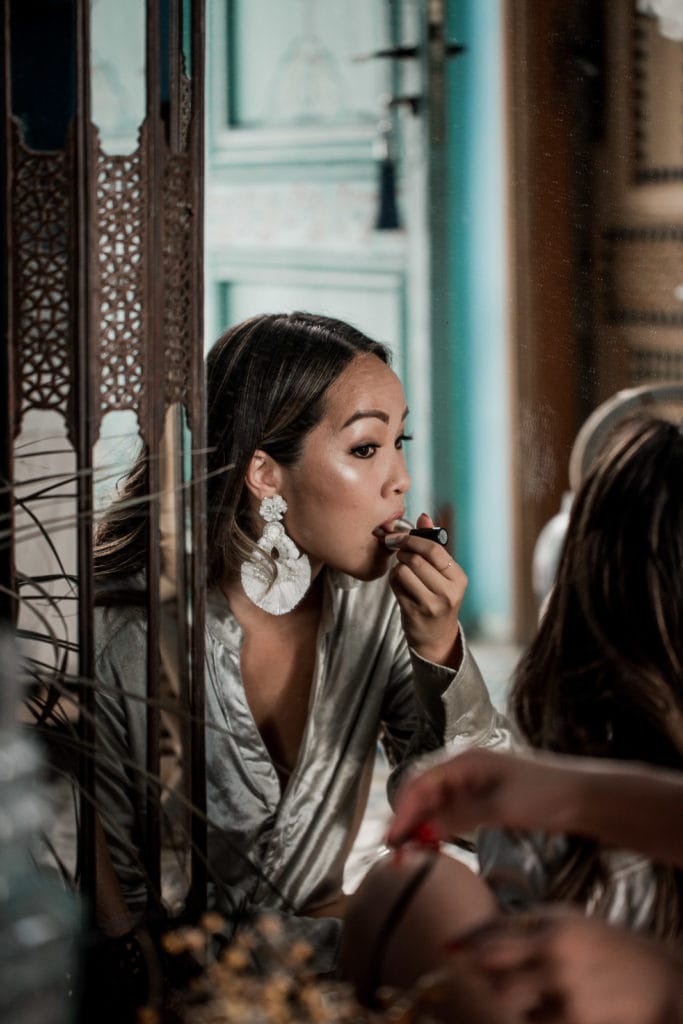 Bride puts on lipstick in mirror as she gets ready for her Marrakech destination wedding