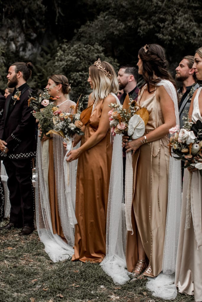 Brides stand together during wedding ceremony in terra cotta and champagne colored bridesmaids dresses