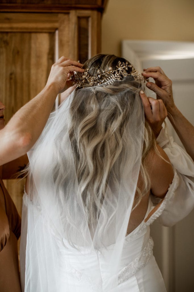 Bridesmaids help bride put in her veil and hair piece as she's getting ready