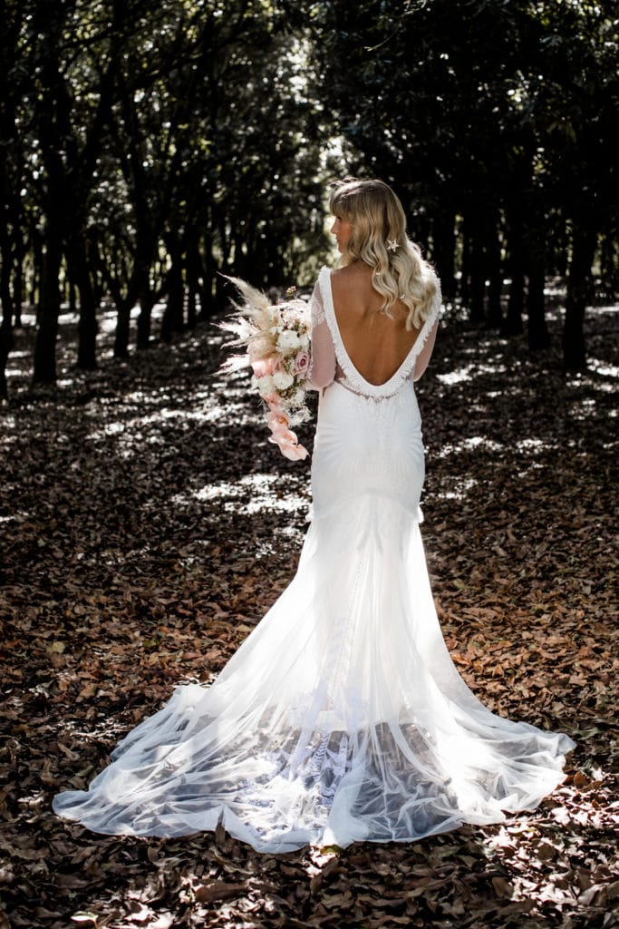 Bride shows back of her bohemian-chic gown during bridal portraits
