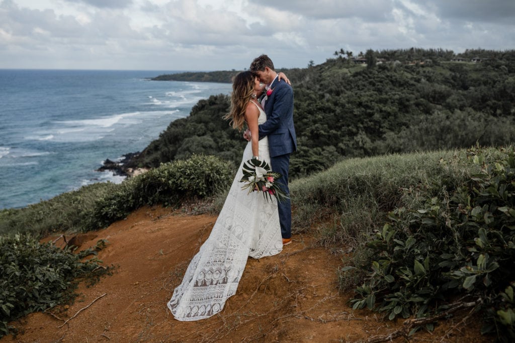 Bride and groom stand together for portraits overlooking Hawaii coastline