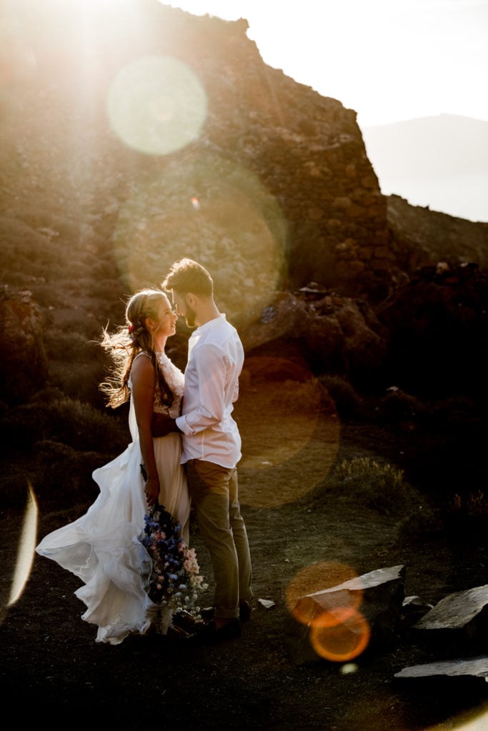 Bride and groom embrace during couple's portraits at sunset on cliffsides of Greece