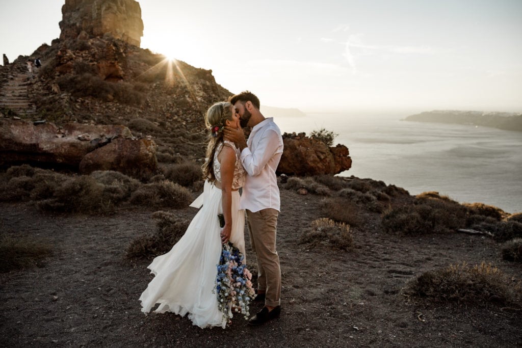 Bride and groom kiss during sunset portraits on the Greek cliffsides after their Santorini elopement