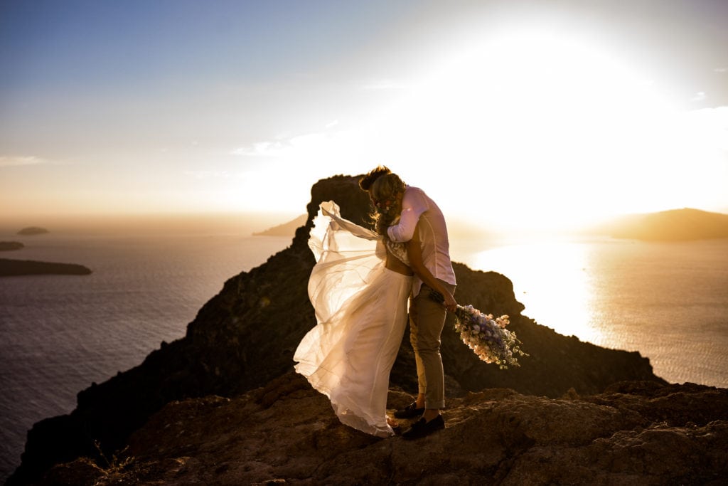 Bride and groom stand together on Santorini cliff at sunset for portraits