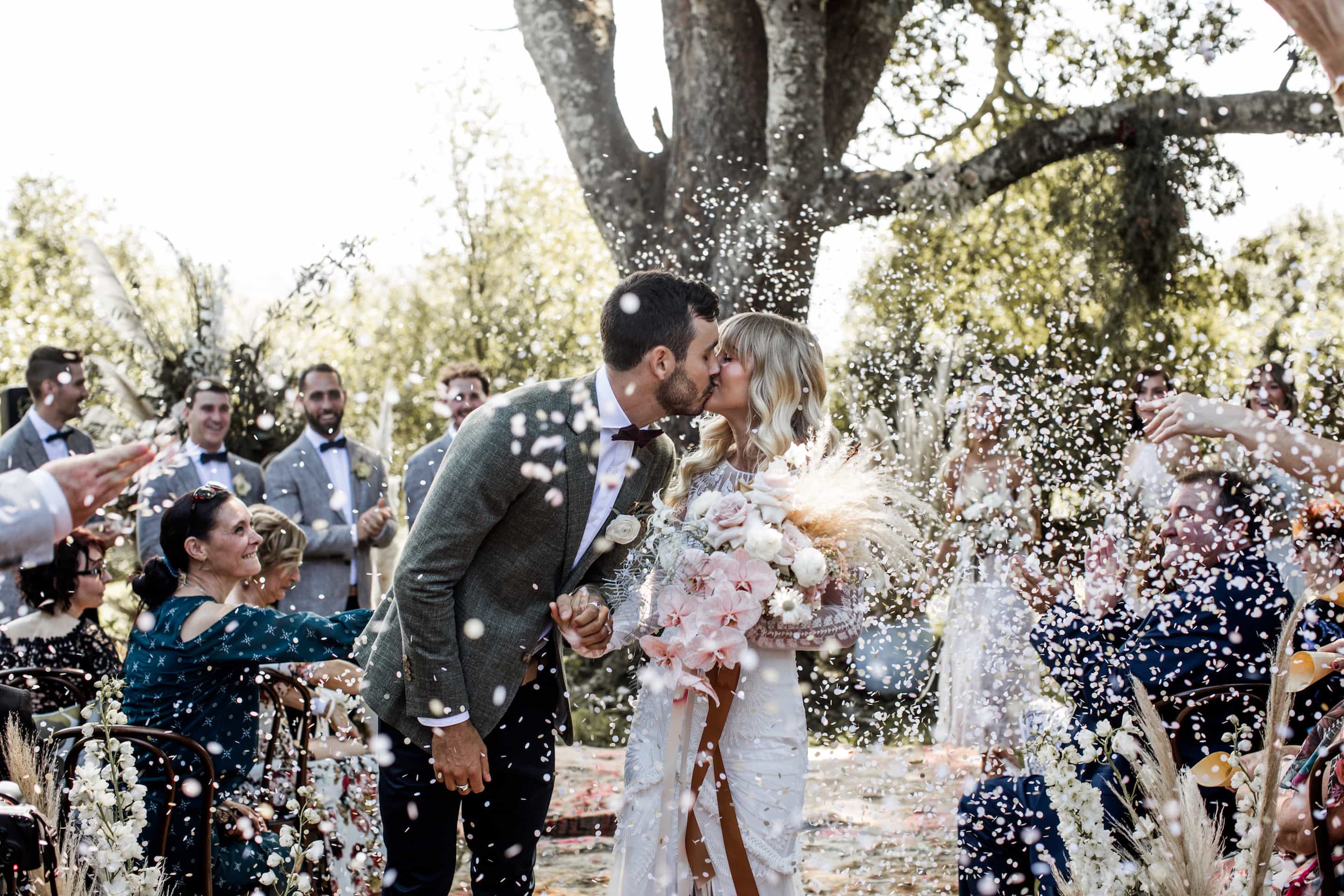 Bride and groom kiss after their Byron Bay wedding ceremony as guests throw flower petals for their exit