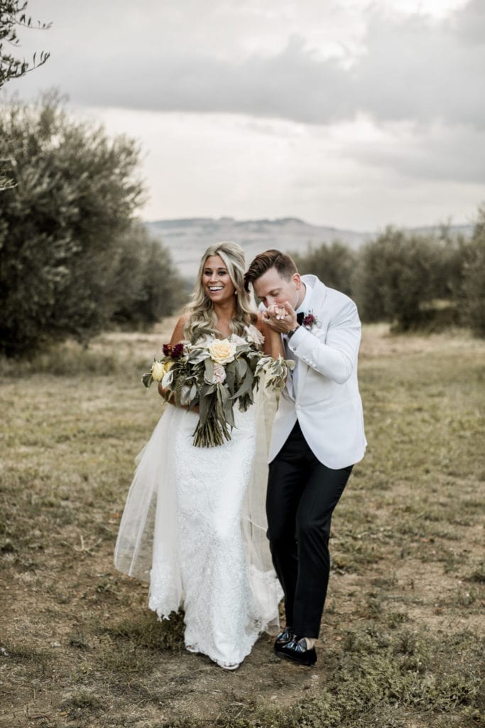 Groom kisses bride's hand during couple's portraits after destination wedding ceremony in Tuscany