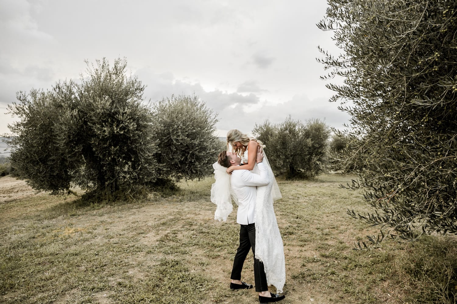 Groom lifts bride during couple's portraits after destination wedding in Tuscany, Italy