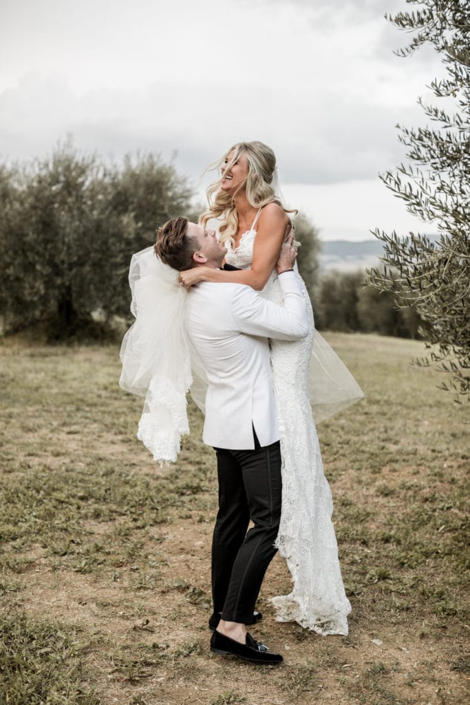 Groom lifts bride up during portraits after destination wedding in Tuscany, Italy