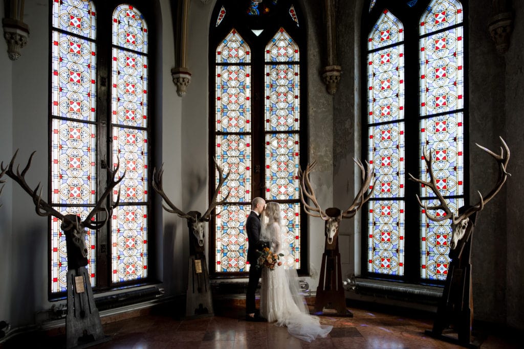 Bride and groom stand in front of stained glass windows at Vajdahunyad Castle in Budapest, Hungary