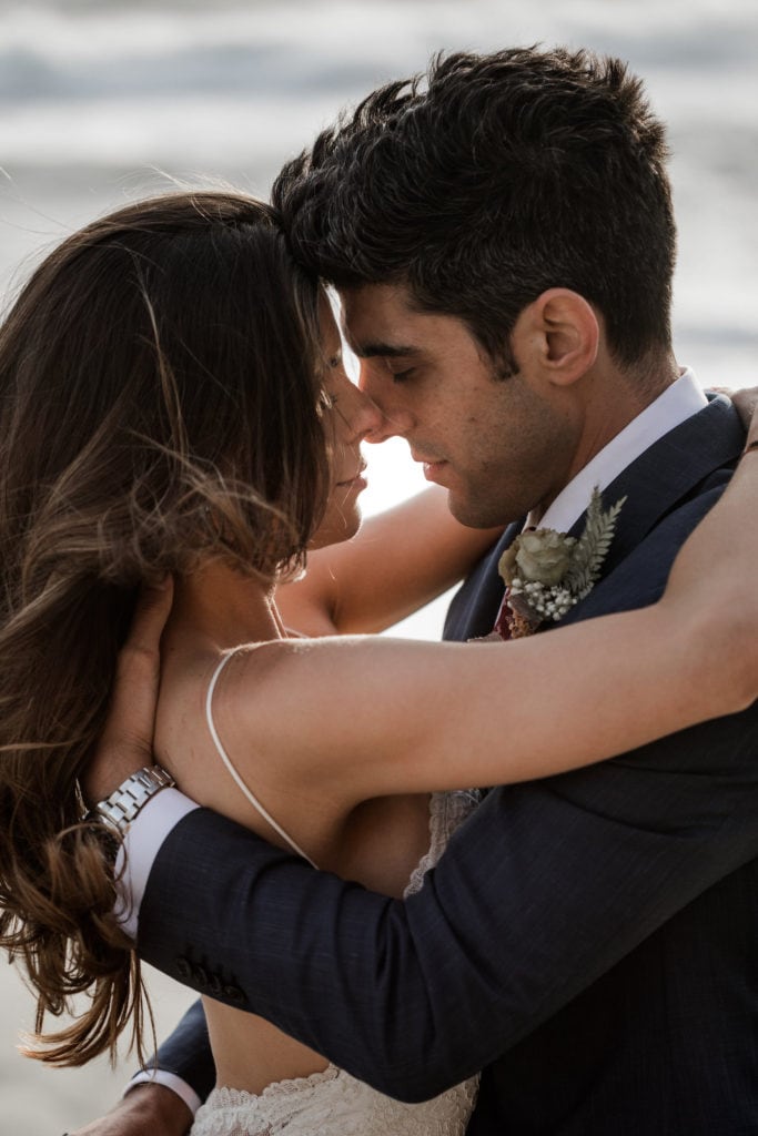 Bride and groom share intimate hug during couple's portraits on California beach at sunset