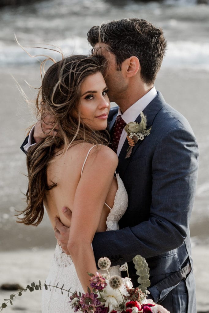 Bride and groom pose together during couple's portraits on a California beach