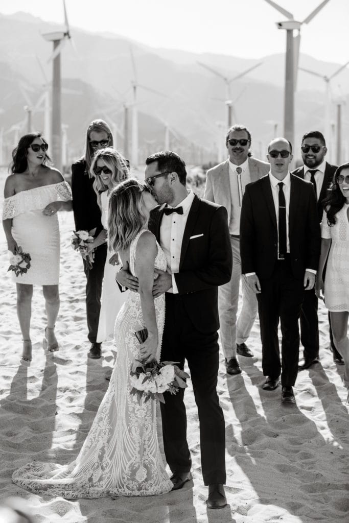Bride and groom kiss with bridal party in background in Palm Springs desert