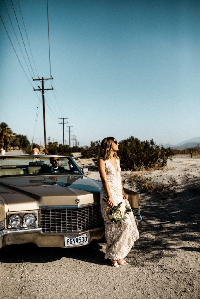Bride leaning against cadillac while groom sits in car