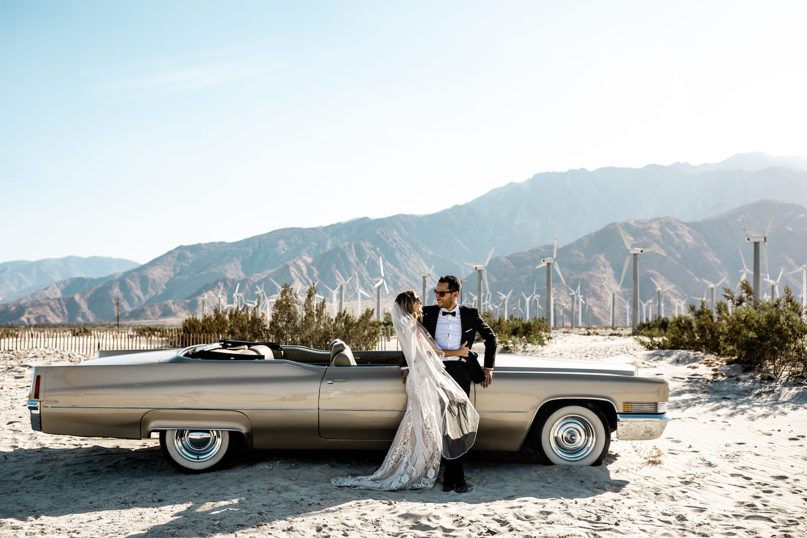 Bride and groom stand together next to classic Cadillac in Palm Springs, California