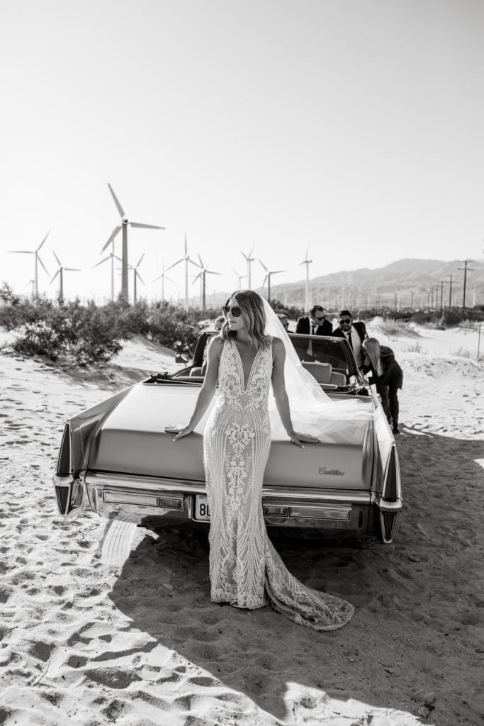 Bride wearing bridal gown leans against classic Cadillac in Palm Springs California