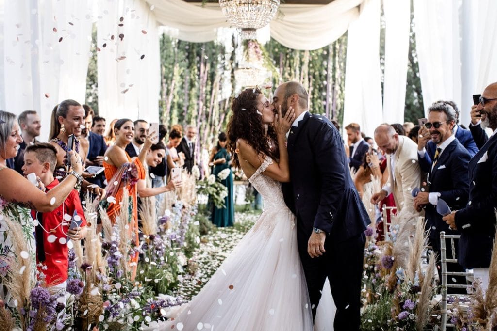 Bride and groom kiss at end of wedding ceremony aisle in front of guests