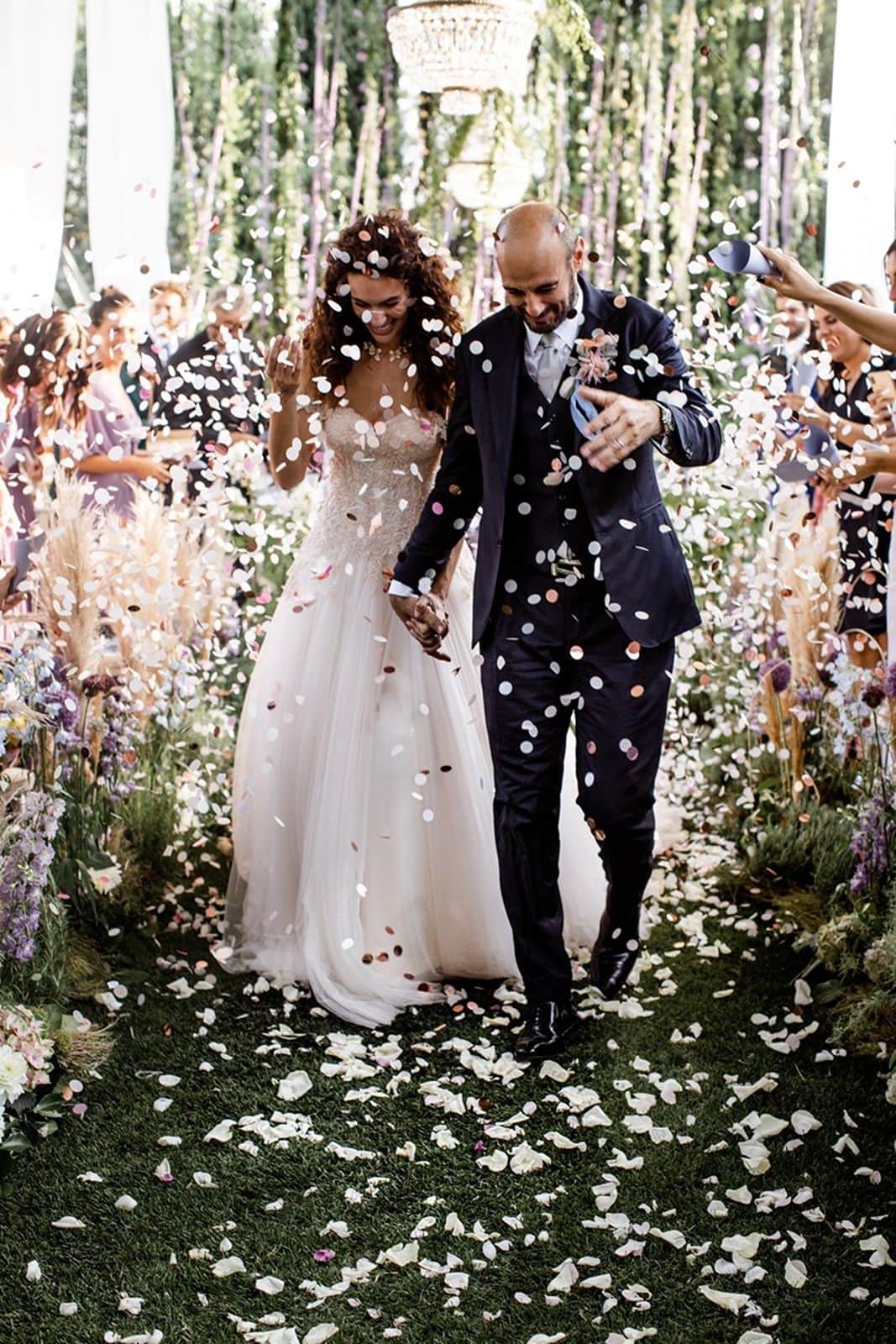Bride and groom walk down Italian garden wedding ceremony aisle while guests toss confetti