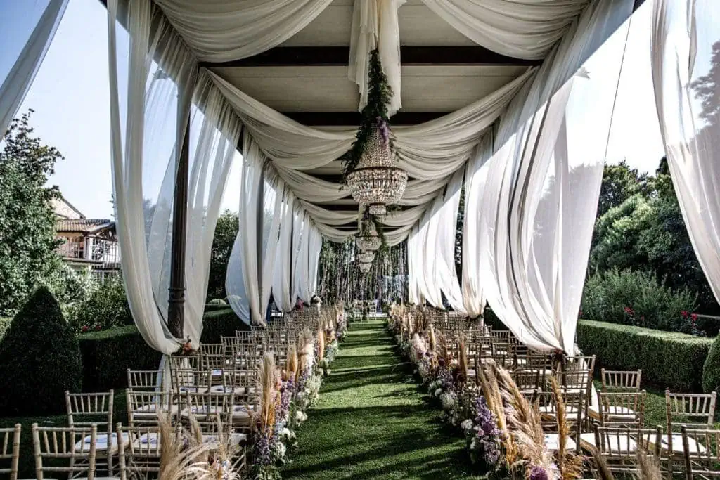 Italian garden wedding ceremony setup with drapery and chandeliers hanging from tent