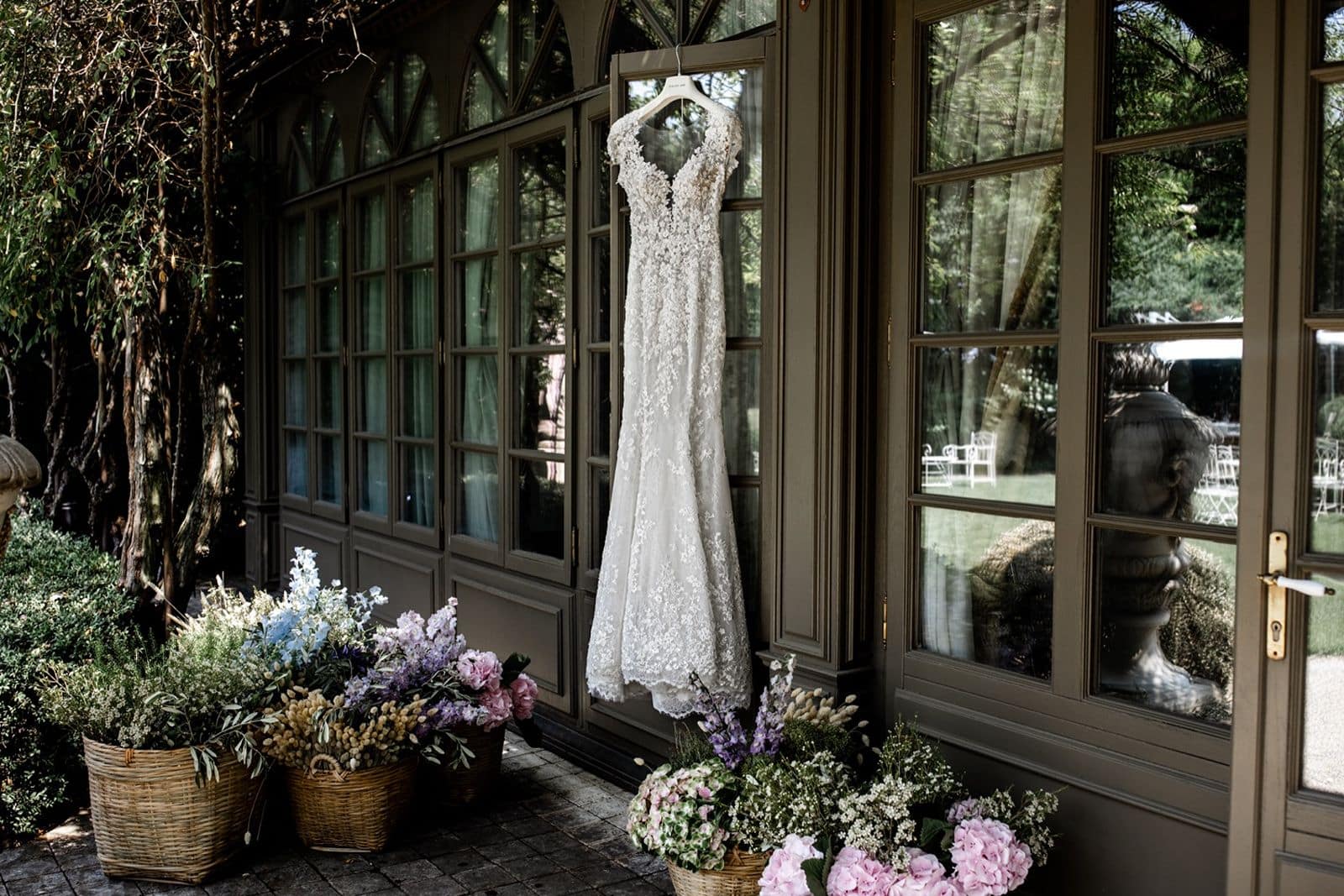 Lace wedding gown hangs in front of windows at an Italian garden wedding venue