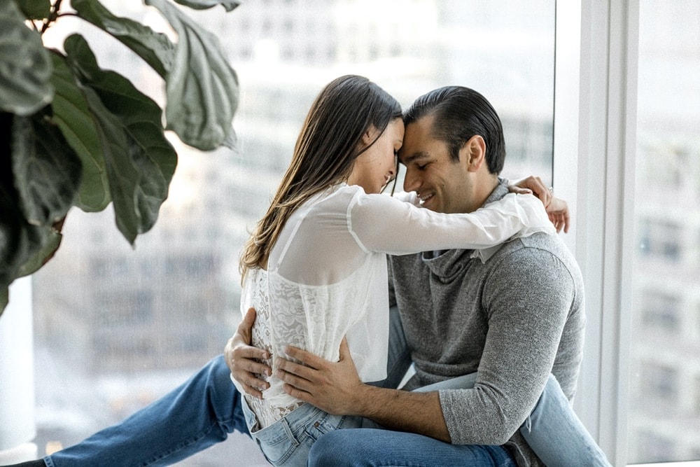 Couple sit on windowsill with view of New York City in background