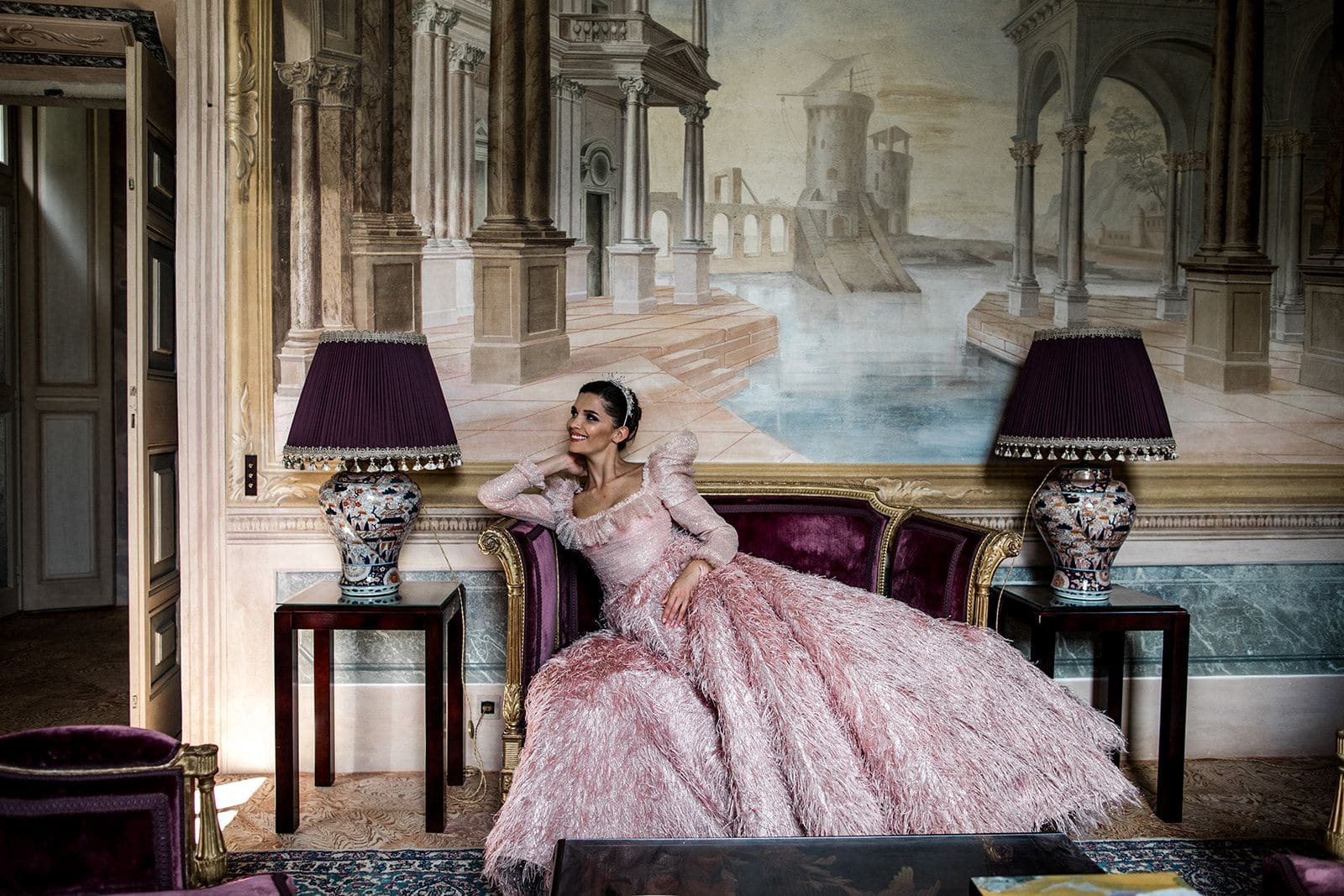 Bride in pink feather ball gown sits on sette in Villa Balbiano
