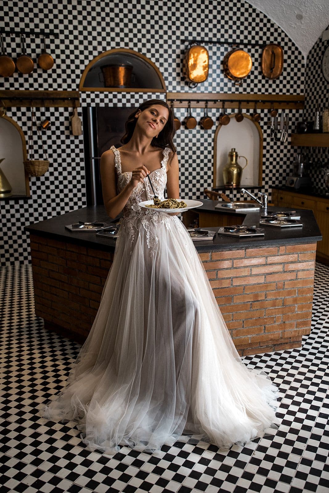 Bride wearing Berta bridal gown stands in kitchen of Villa Astor eating pasta