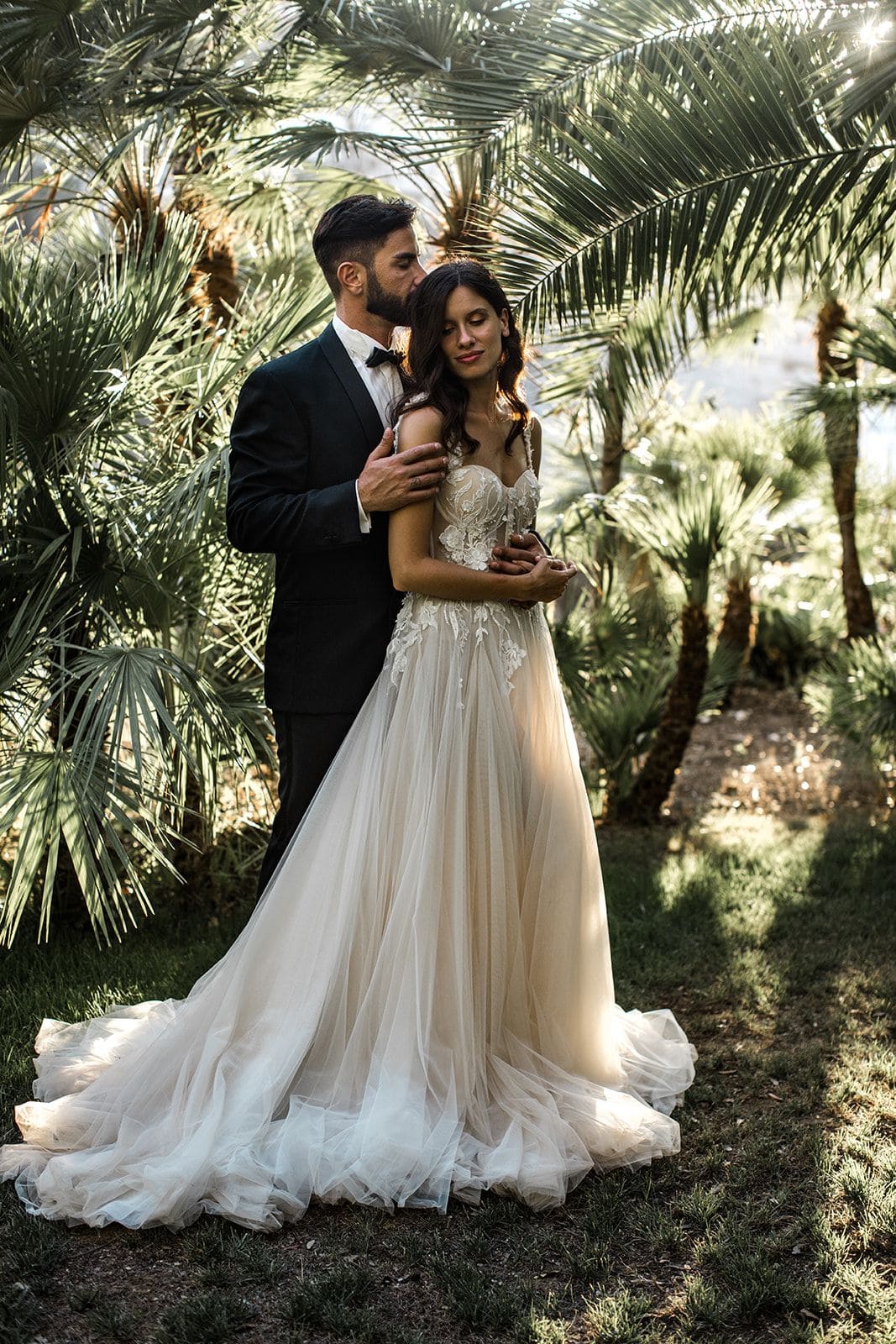 Bride and groom stand together amidst foliage in Villa Astor