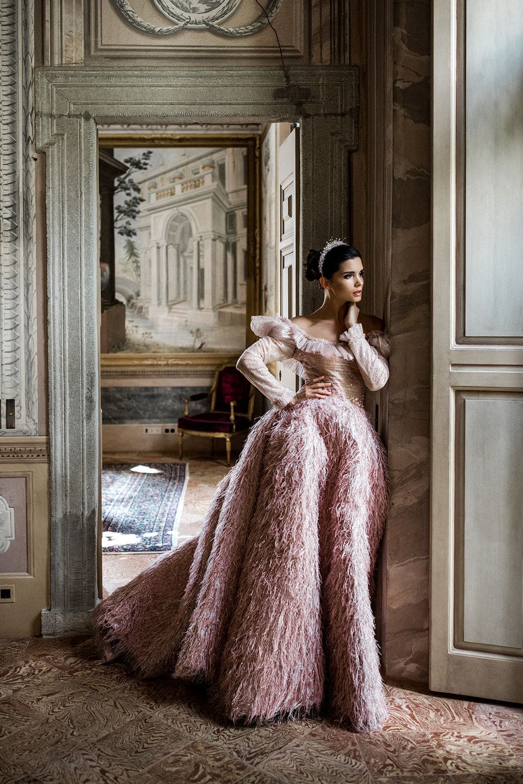 Woman leans in doorway of Villa Balbiano wearing pink haute couture gown with feather skirt
