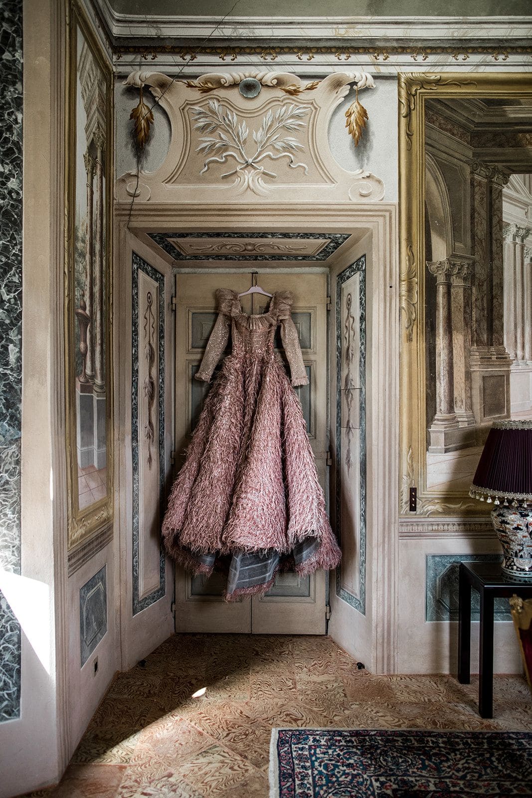 Couture gown hangs on doorway amidst Villa Balbiano's ornate architecture