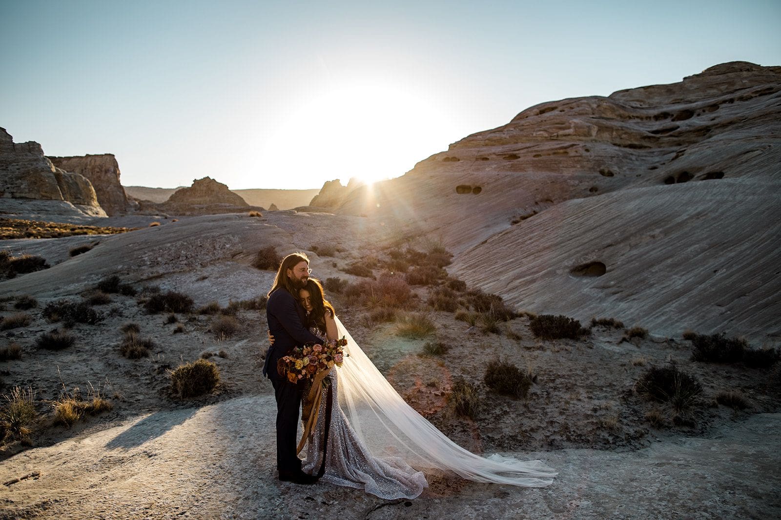 Bride and groom embrace in Utah desert as the sun sets
