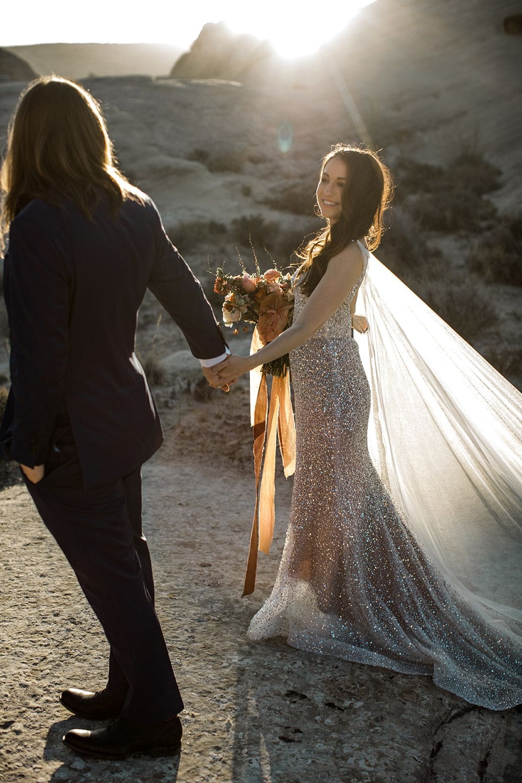 Bride and groom walk through Utah desert as the sun sets