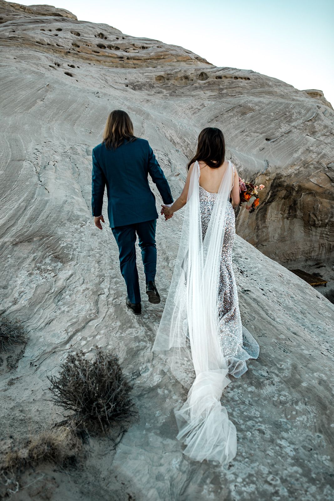Bride and groom walk up plateau in Utah desert