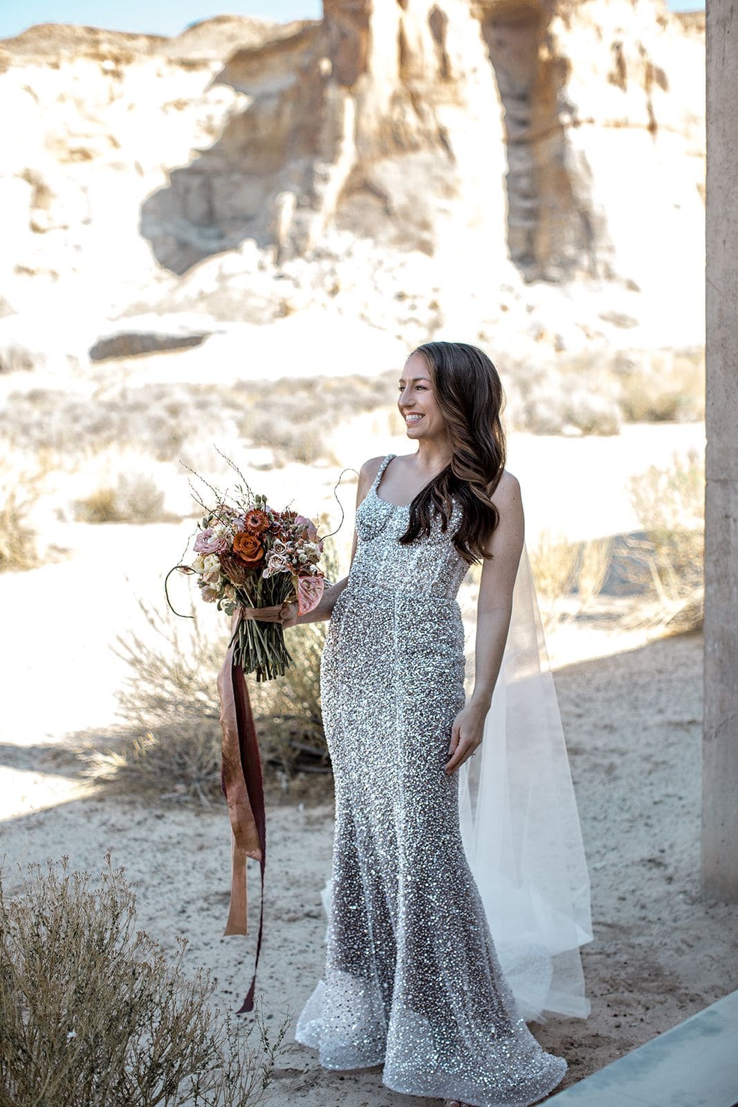 Bride wears sparkling fitted silhouette gown and holds bridal bouquet