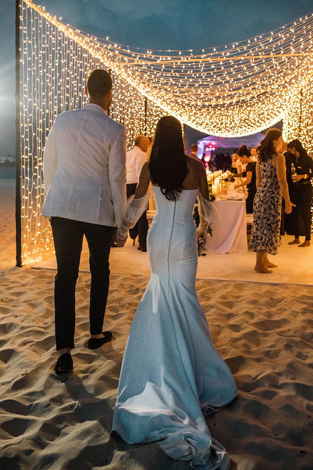 Bride and groom walk to their wedding reception under a light tunnel on the beach of Anguilla