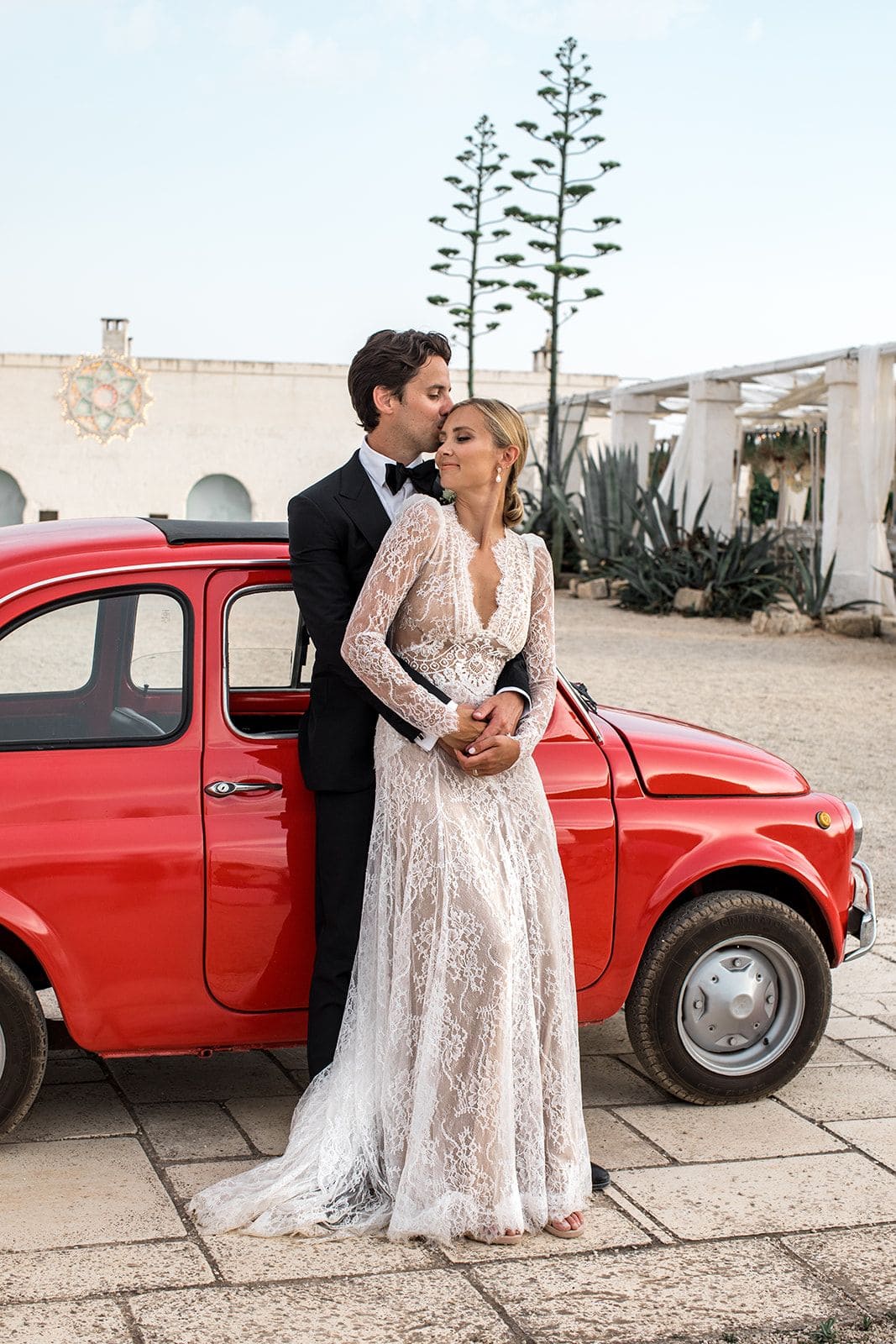 Bride groom against small red car in Puglia Italy