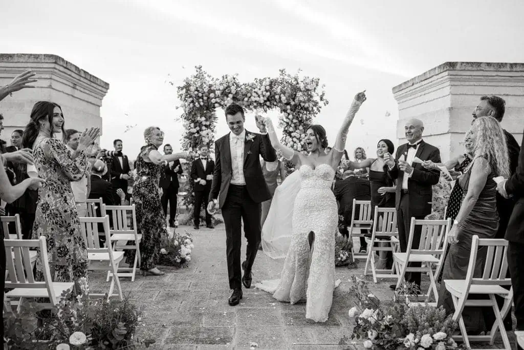 A black and white portrait of a bride and groom walking together down the aisle after getting married. 