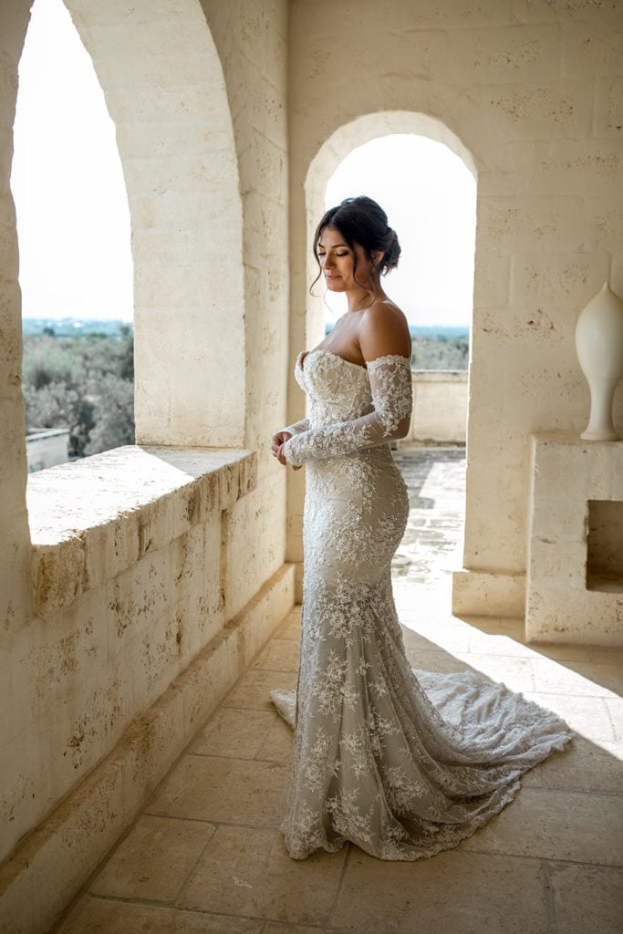 A bride, dressed in her bridal gown, watches out the windows of the Terrazza Quattro Torri on her wedding day. 