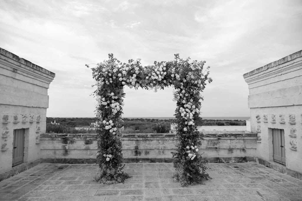 A black and white portrait of a grand ceremony arch with the Adriatic Sea in the background. 