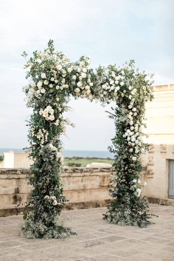 A grand arch is designed with white and cream colored flowers and greenery. 