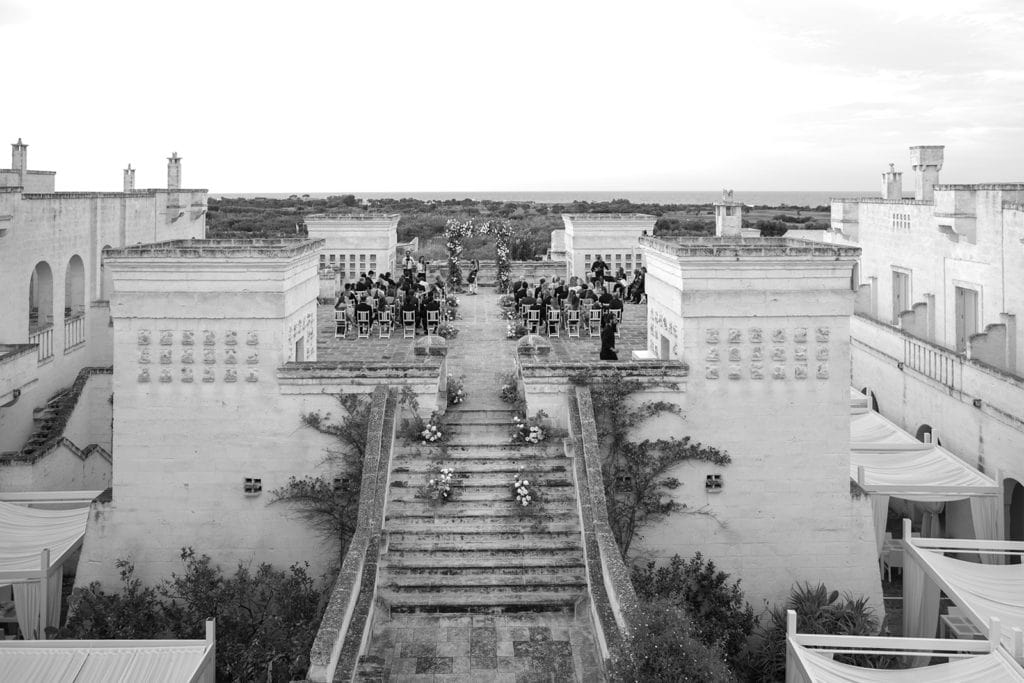 Friends and family sit at a wedding ceremony site, which is on top of the Borgo Egnazia in Puglia, Italy. 