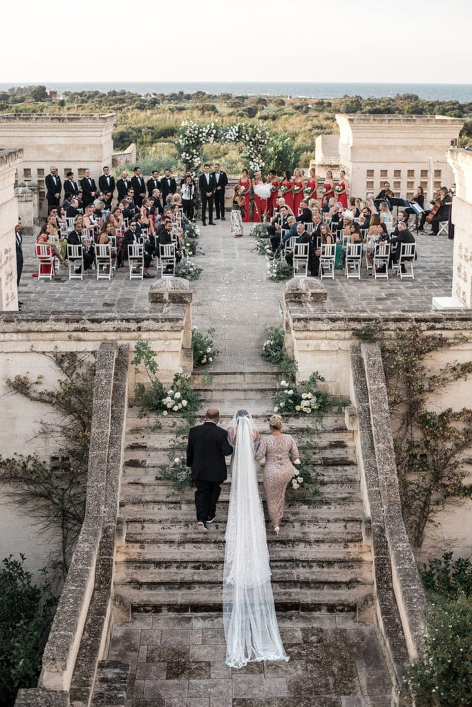 A bride walks with her parents up the steps of her venue in Puglia, Italy. 