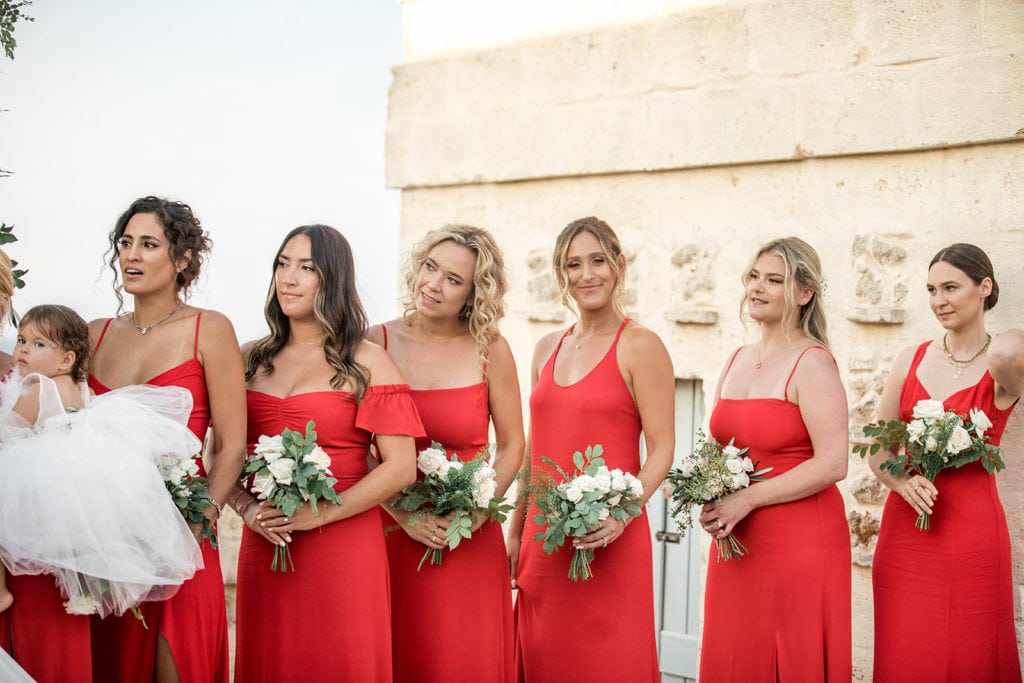 Bridesmaids stand together during a Borgo Egnazia wedding ceremony wearing bright red Reformation dresses. 