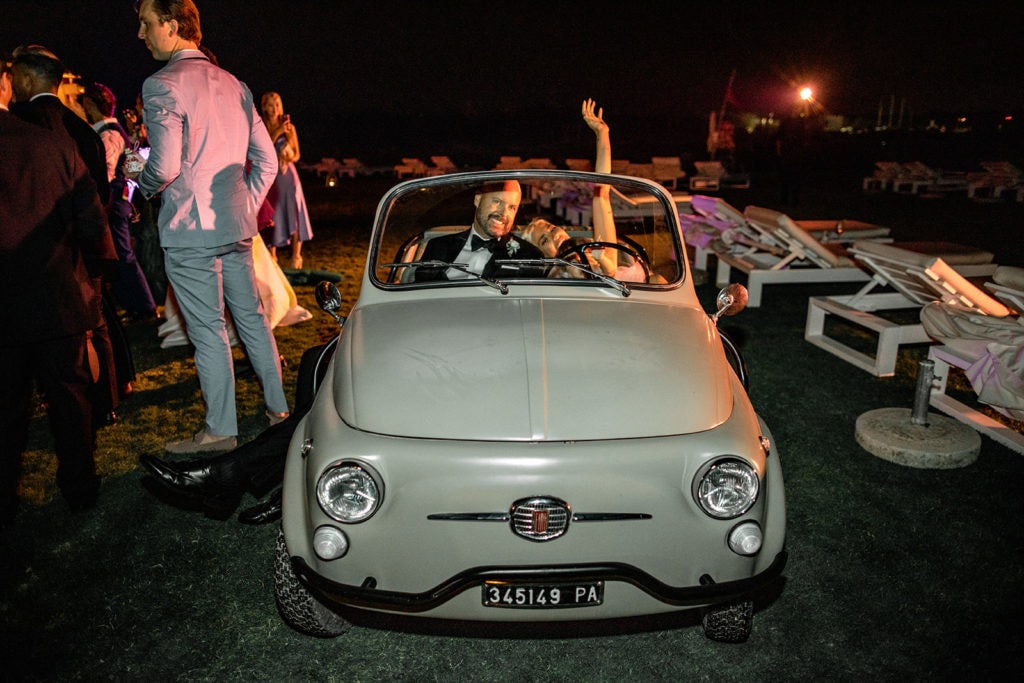 Guests sit in a classic Italian car at a wedding reception. 