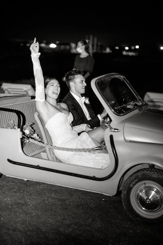 A bride and groom arrive to their wedding reception in a classic Italian car.