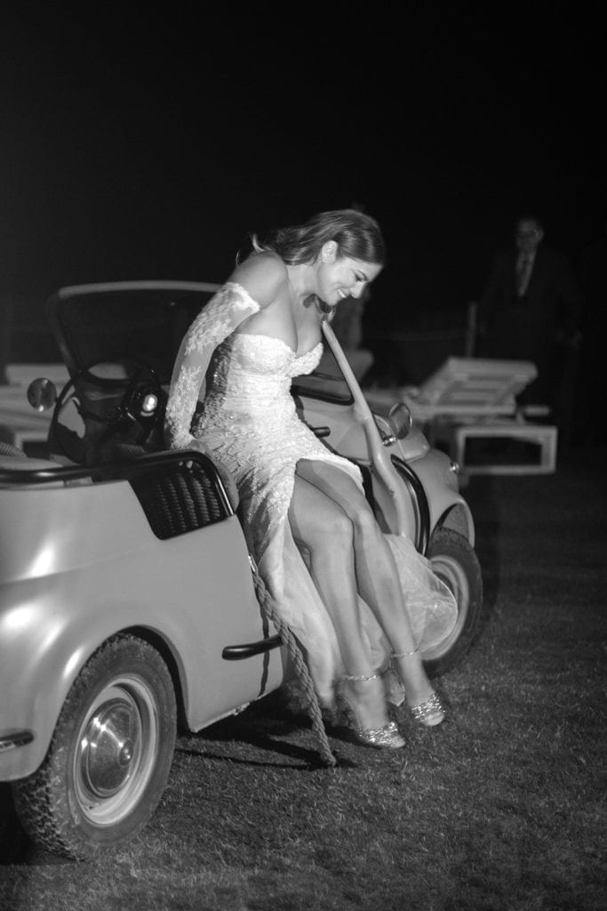 A bride steps out of a classic Italian car at her wedding reception. 