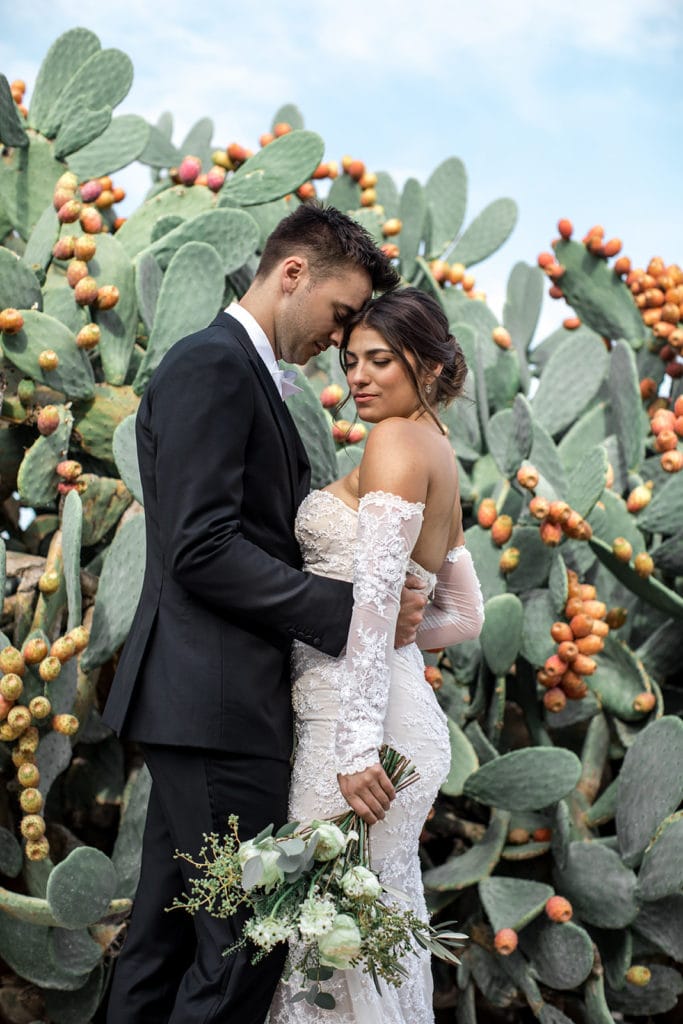 A bride and groom stand among the cacti in Puglia Italy during their Borgo Egnazia wedding. 
