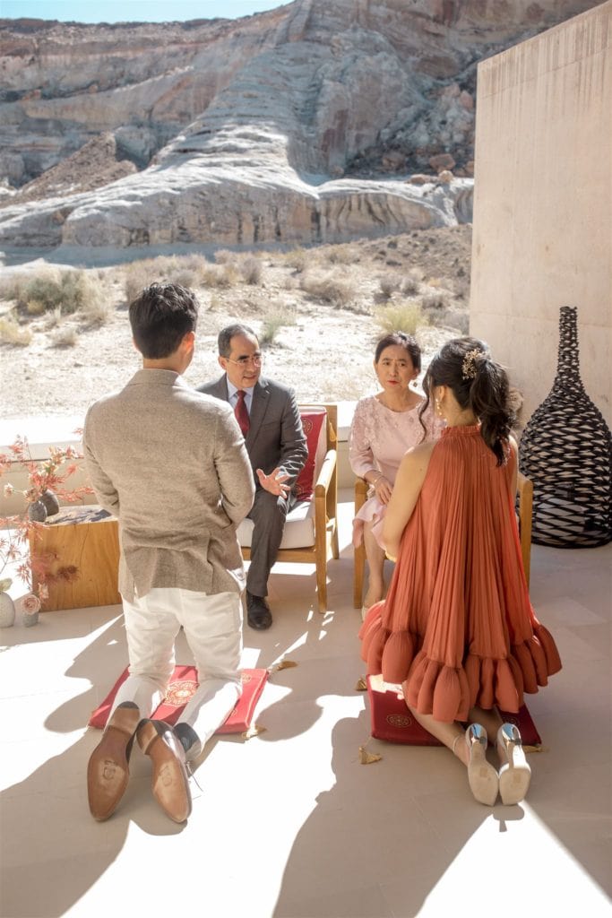 A bride and groom kneel before the groom's parents in a traditional tea ceremony before their Amangiri wedding. 