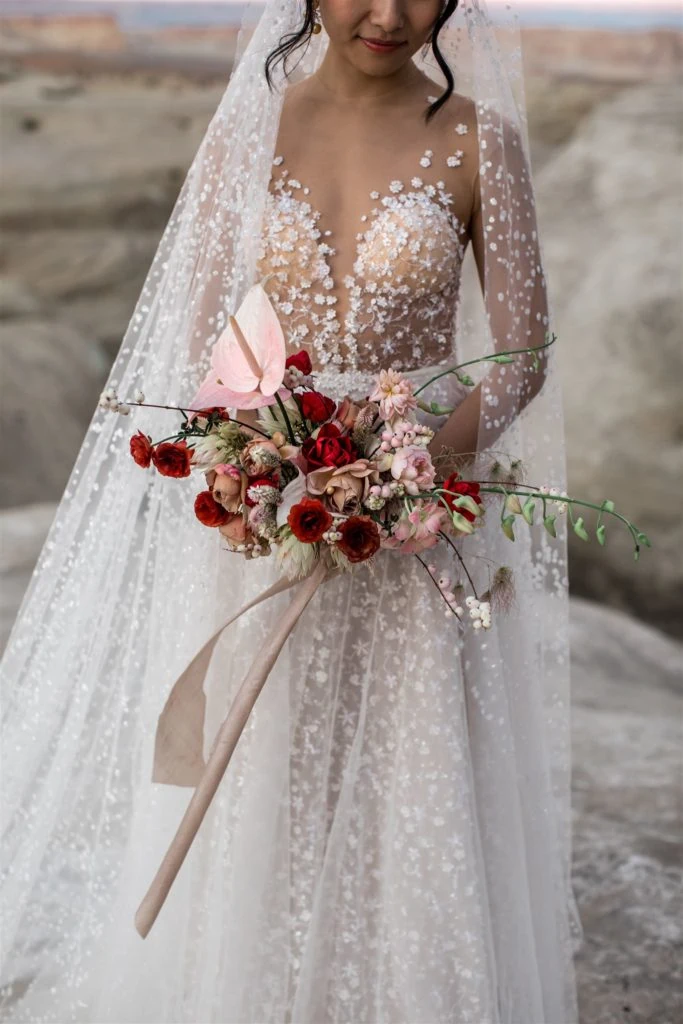 A bride wears a Berta detailed gown while holding a bouquet of red and pink roses. 